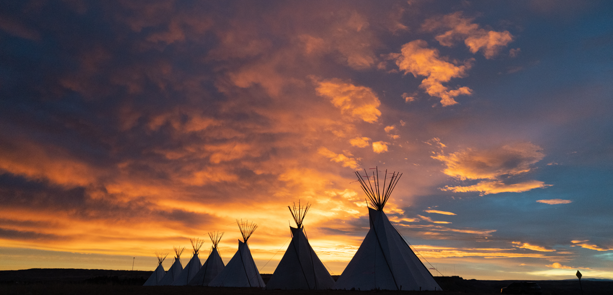 Photo: View of tipis against the backdrop of a sunrise.