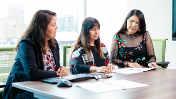 Three Indigenous women reviewing documents at a table