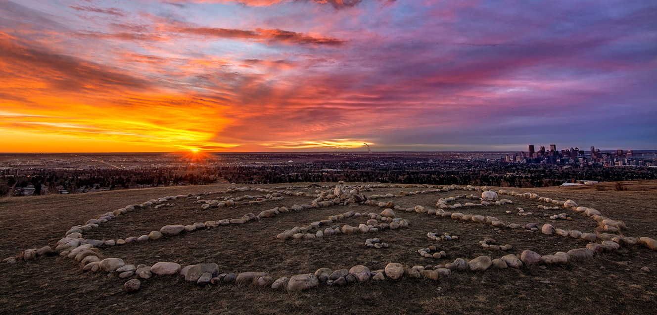 A medicine wheel, crafted from stones and laid out on the ground, takes shape against the backdrop of a sunrise.