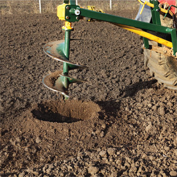 Auger drilling holes in field, preparing for trees planting
